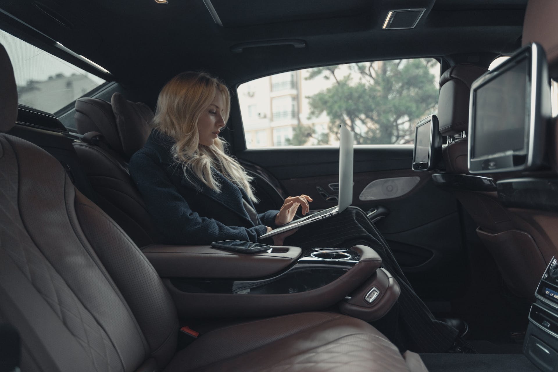 Blonde woman working on a laptop in the back of a taxi