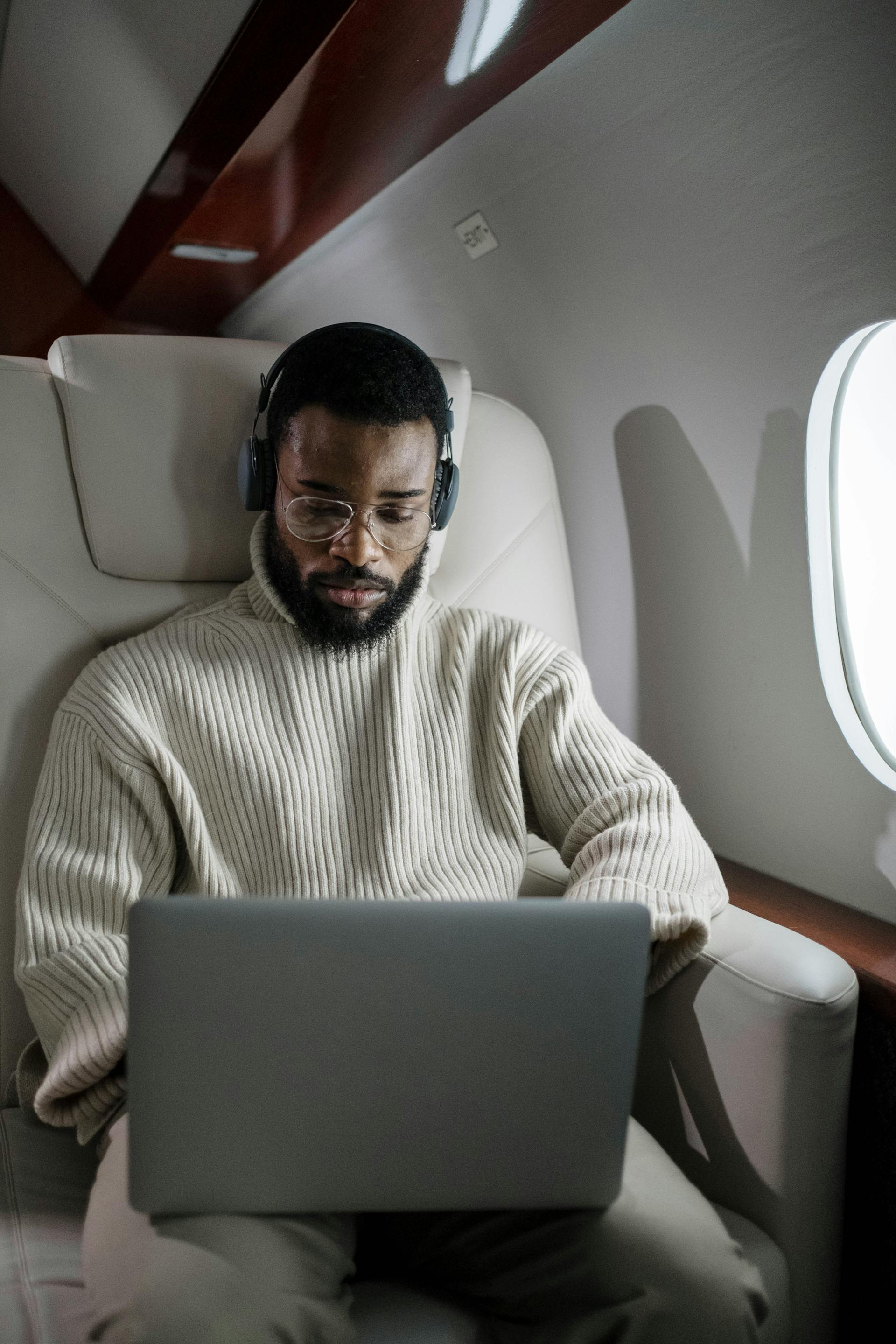 man met koptelefoon en laptop op schoot zittend in en luxe vliegtuig