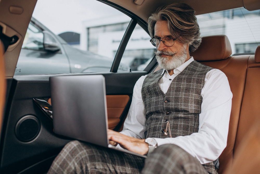 stijlvolle man met laptop op schoot achterin een taxi